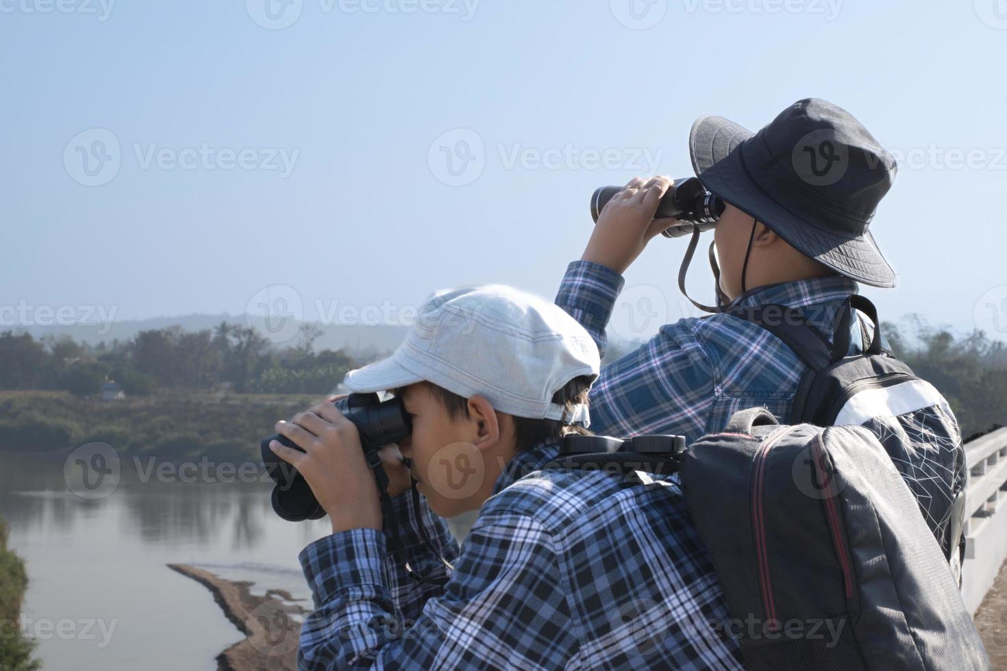 Asian boys are using binoculars to do the birds' watching in tropical forest during summer camp, idea for learning creatures and wildlife animals and insects outside the classroom. photo