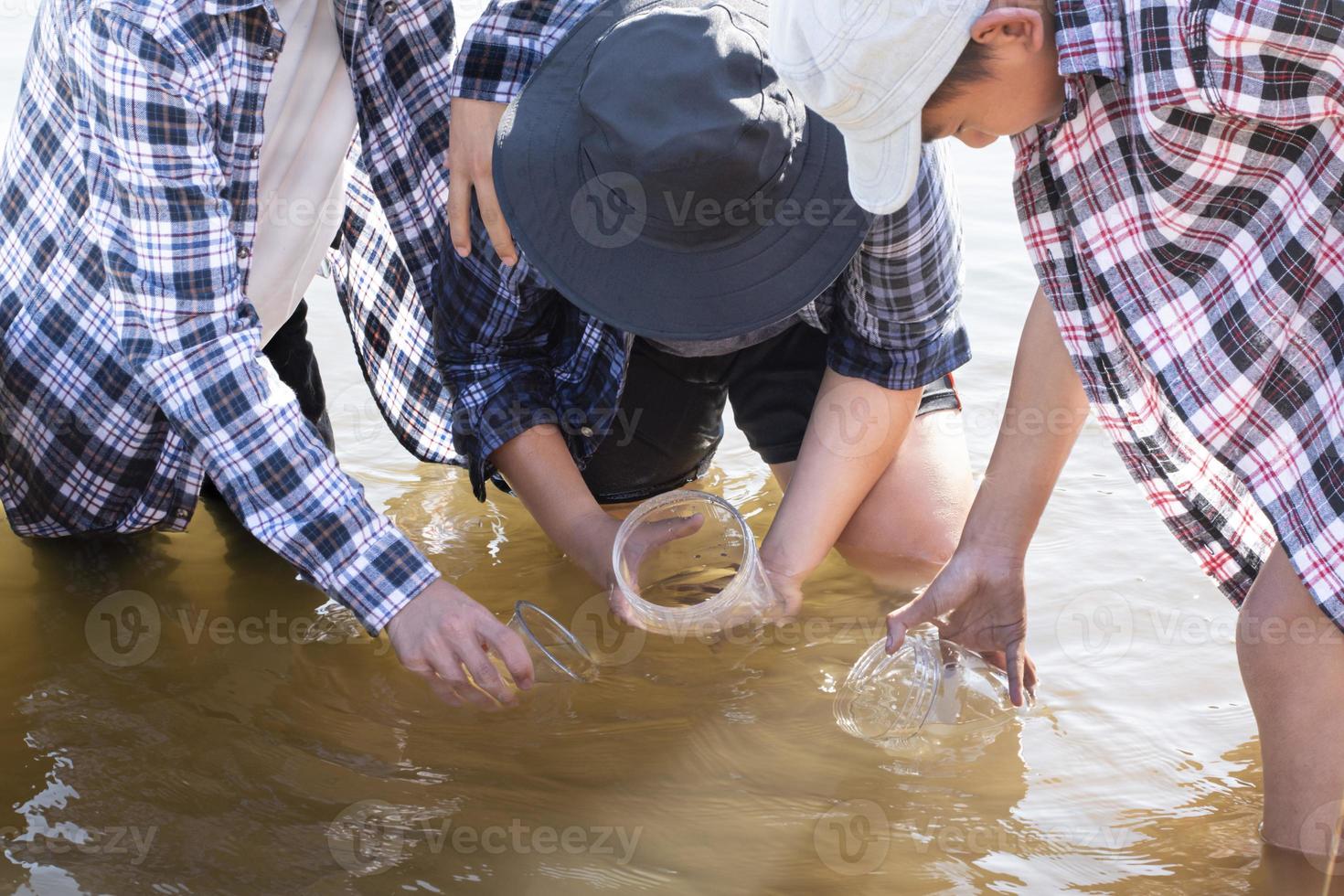 Young asian boy holds transparent tube which has example water inside to do the experiment and ph level measurement as his school project work with his friends behind at the river where he lived. photo