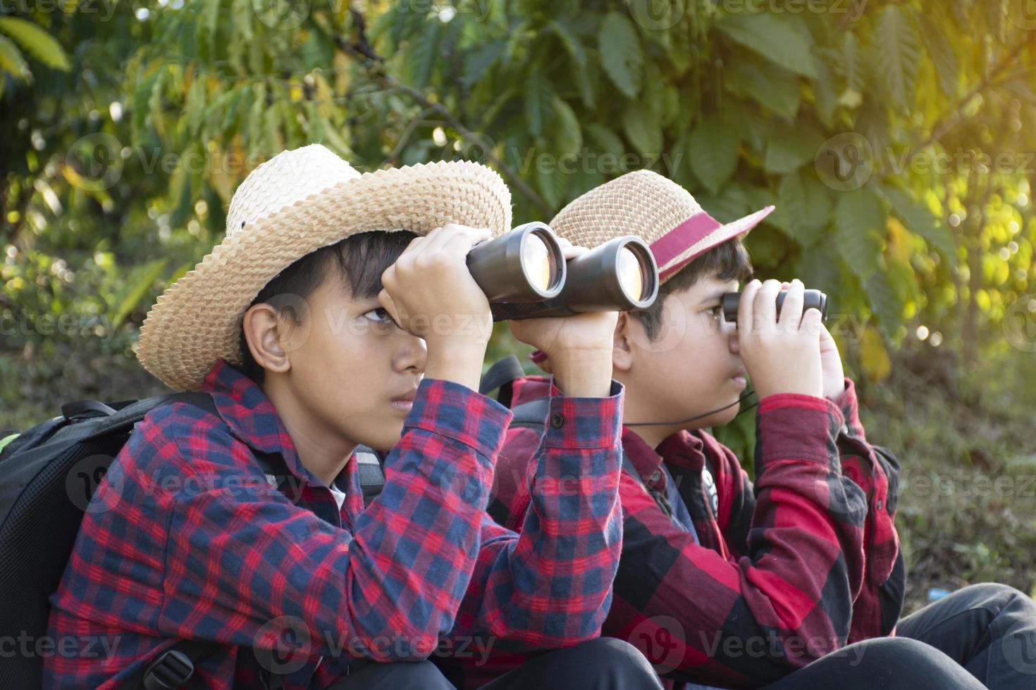 Asian boys are using binoculars to do the birds' watching in tropical forest during summer camp, idea for learning creatures and wildlife animals and insects outside the classroom. photo