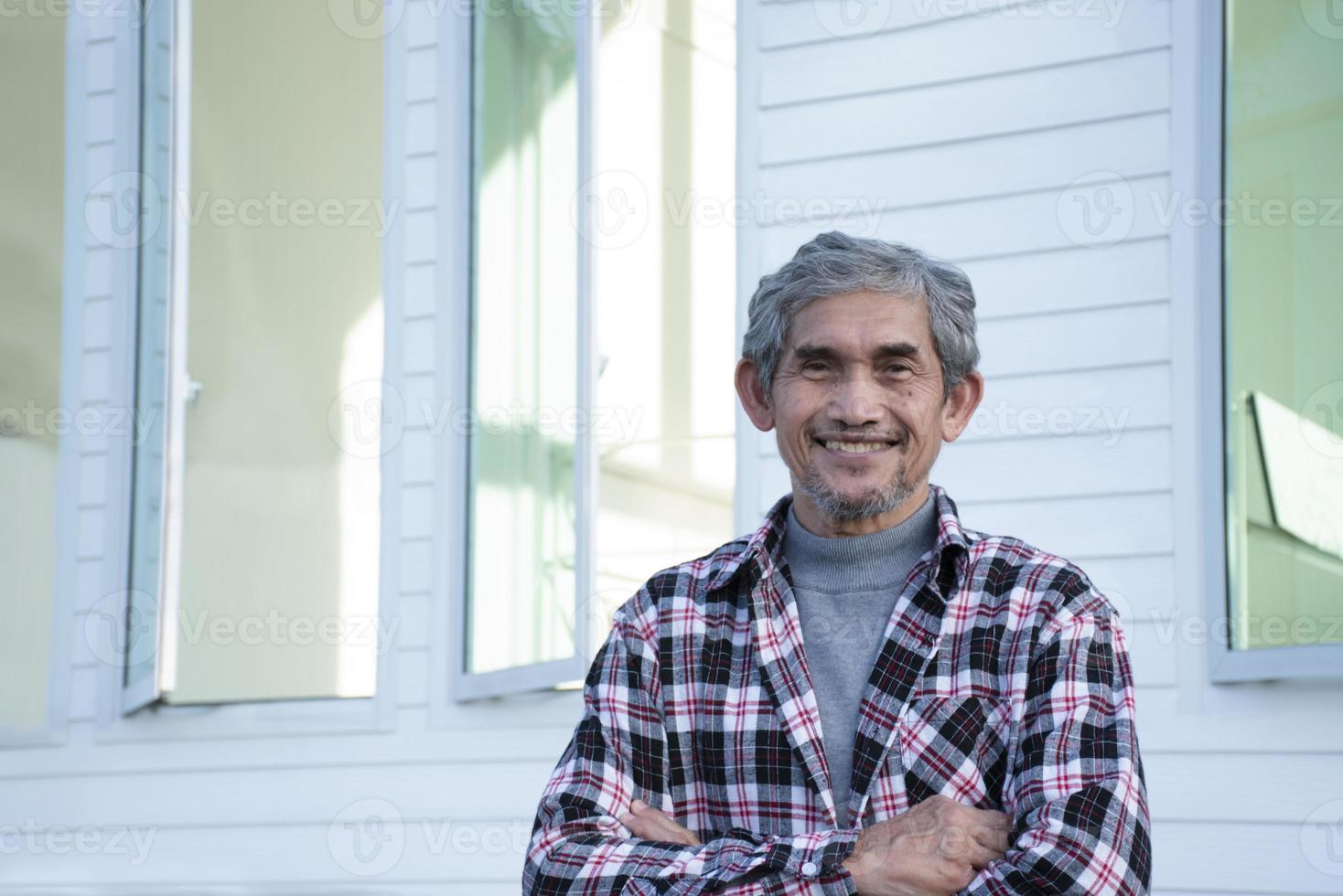 Portrait elderly senior asian man sits near glass window in the morning to work from home and checking his business on his laptop on table seriously, soft and selective focus. photo