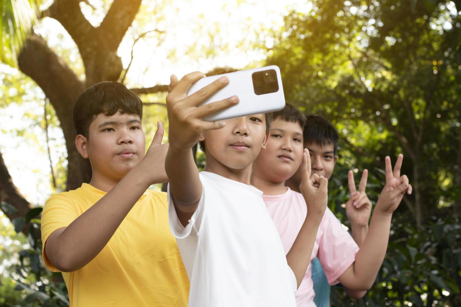 Group of young asian teen boys spending free times in the park rasing their fingers and taking selfie together happily, soft and selective focus on boy in white t-shirt, raising teens concept. photo