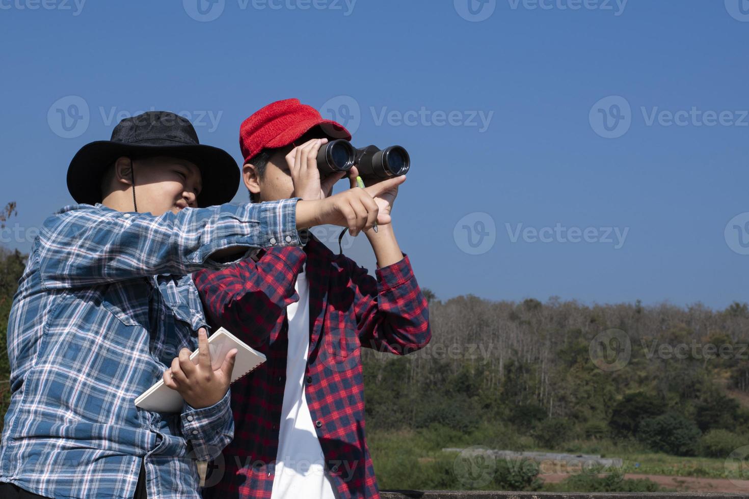 Asian boys are using binoculars to do the birds' watching in tropical forest during summer camp, idea for learning creatures and wildlife animals and insects outside the classroom. photo