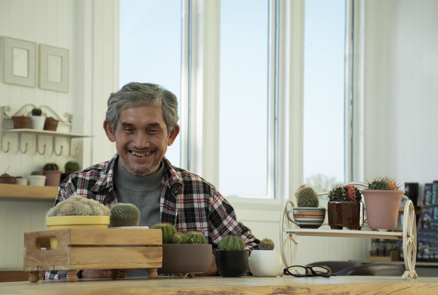 retrata a un anciano asiático sentado cerca de una ventana de vidrio por la mañana para trabajar desde casa y revisando su negocio en su computadora portátil en la mesa con seriedad, enfoque suave y selectivo. foto