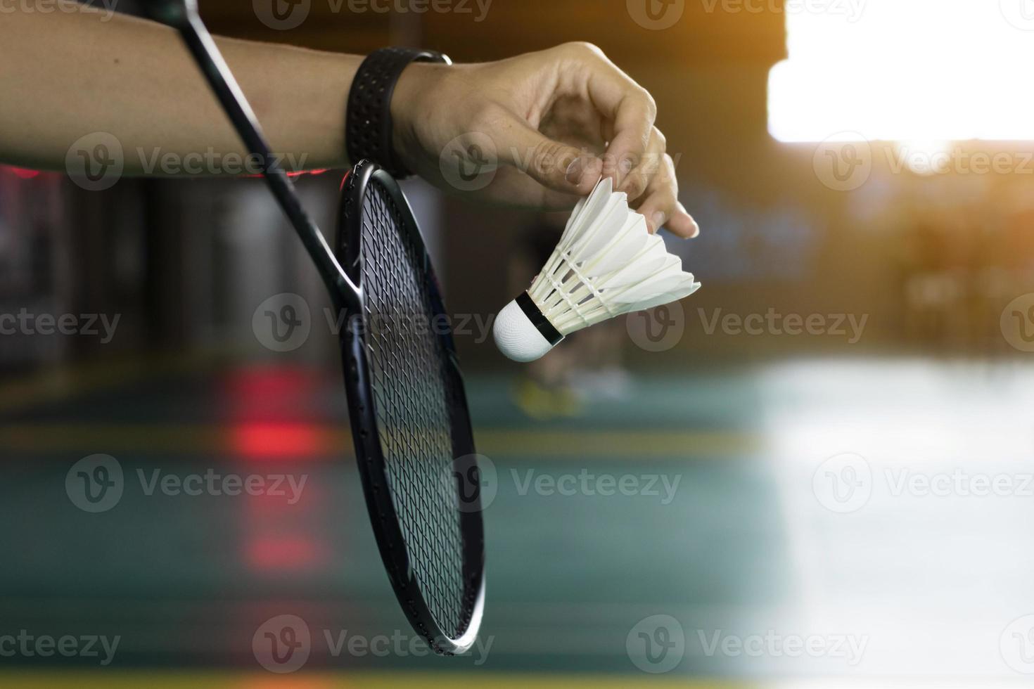 Badminton player holds white cream shuttlecock and racket in front of the net before serving it to another side of the court, soft and selective focus on shuttlecock. photo