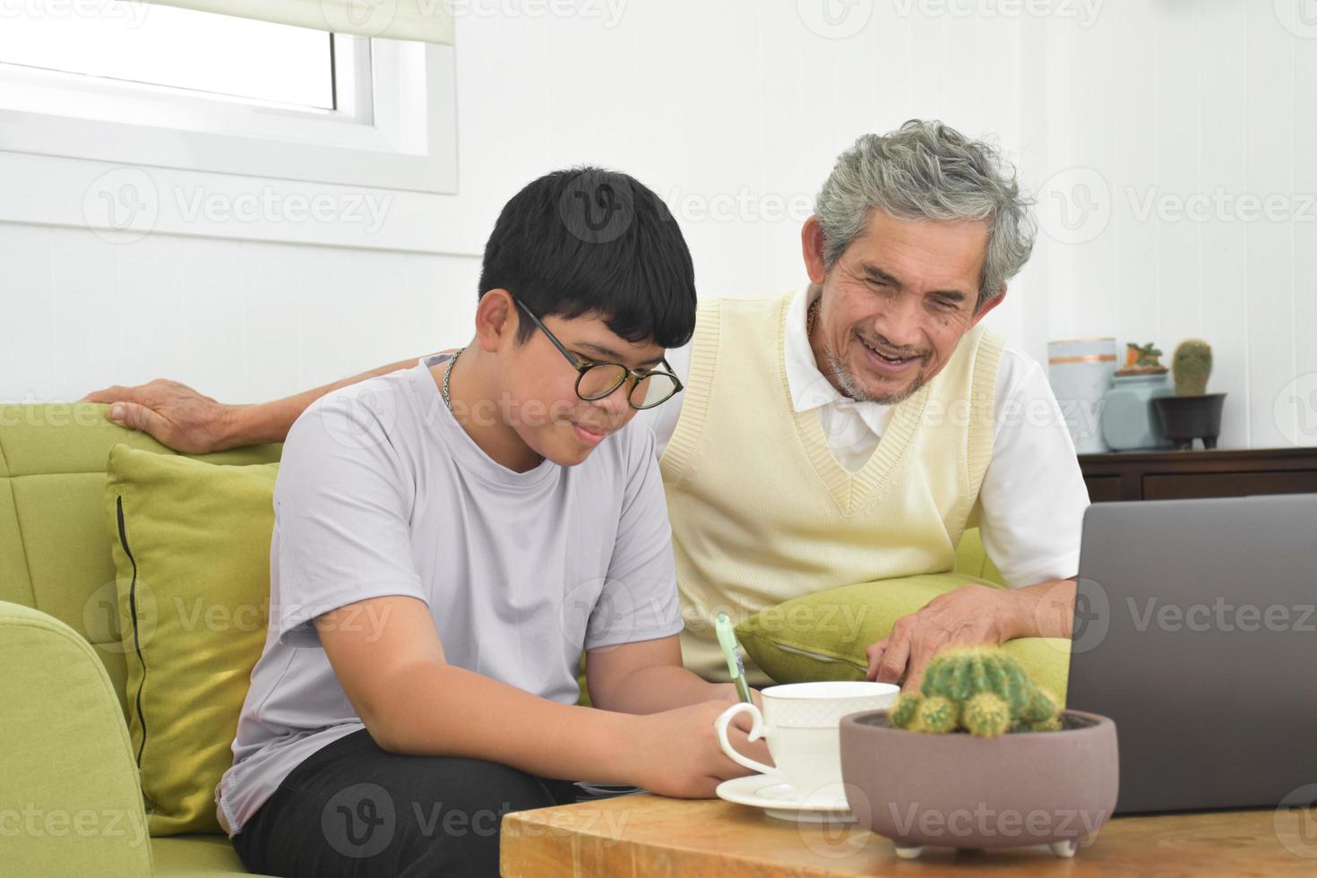 el abuelo mayor asiático y su hijo pasan tiempo juntos en casa para conectar los auriculares con su computadora portátil para ver y jugar juegos en línea, enfoque suave y selectivo, elevando el concepto de adolescentes. foto