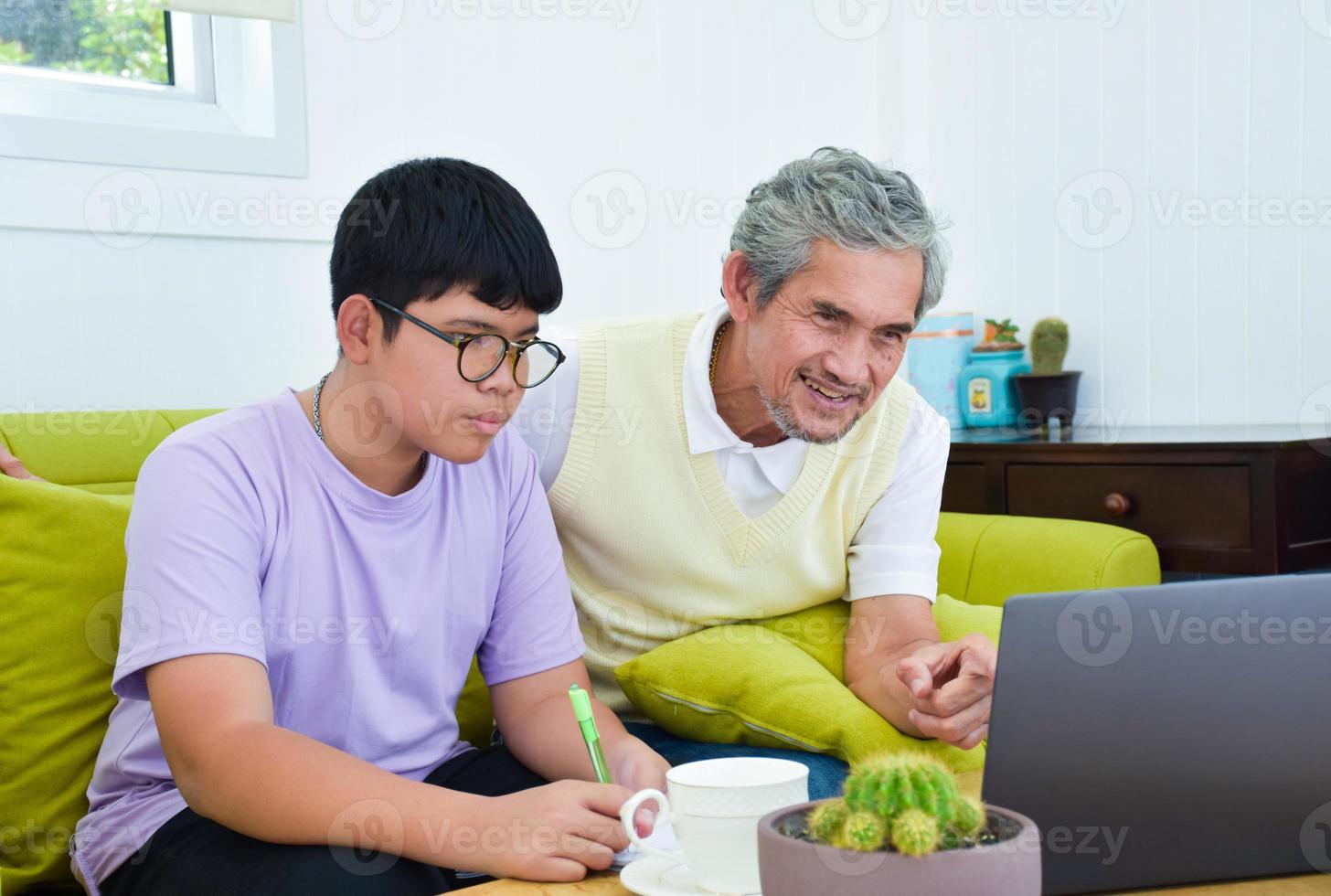 Asian senior grandpa and his son are spending times together at home to connect headphone with his laptop to watch and to play online games, soft and selective focus, raising teens concept. photo