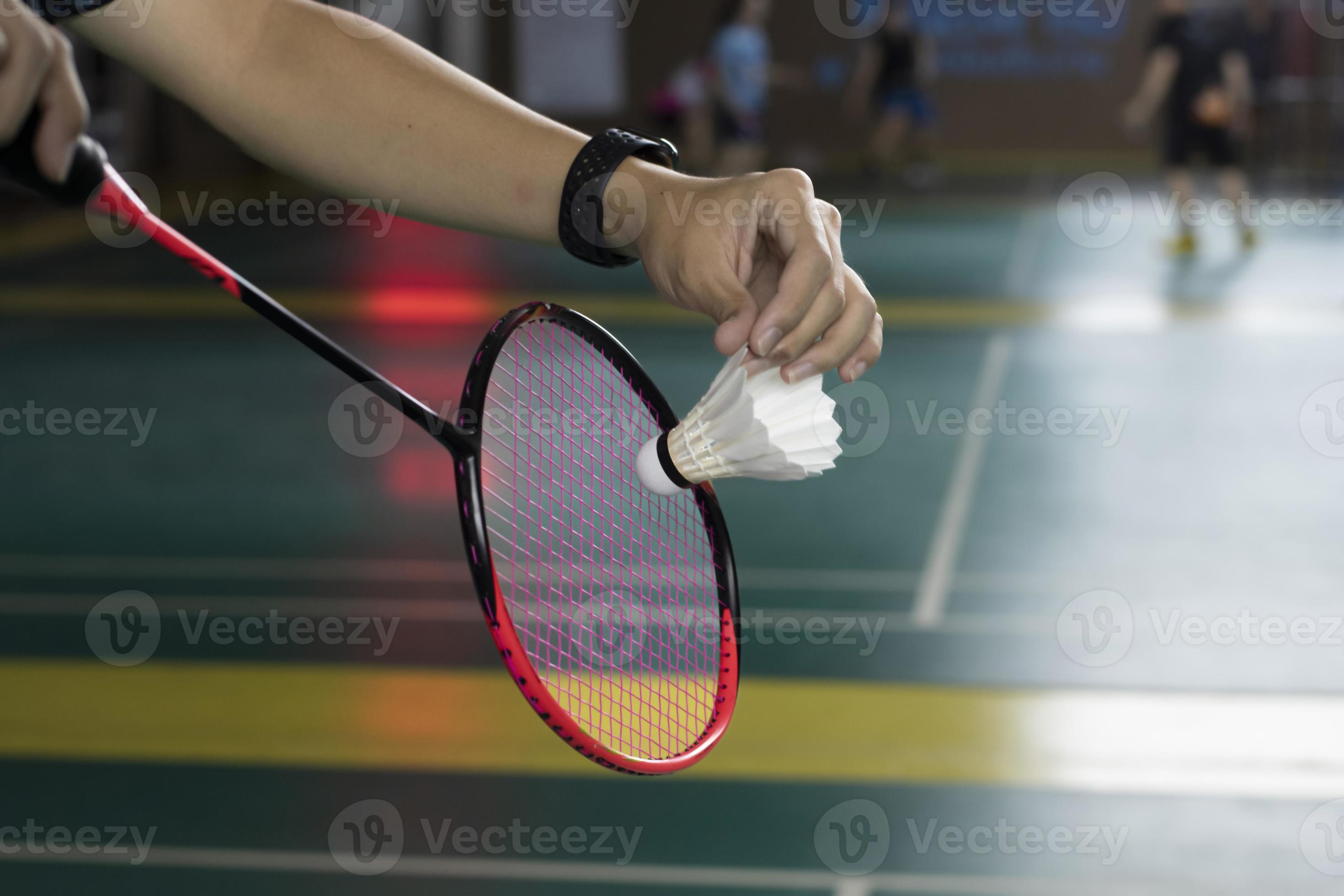Badminton player holds white cream shuttlecock and racket in front of
