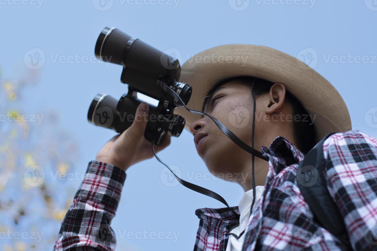 Asian boy is using binoculars to do the birds' watching in tropical forest during summer camp, idea for learning creatures and wildlife animals and insects outside the classroom. photo