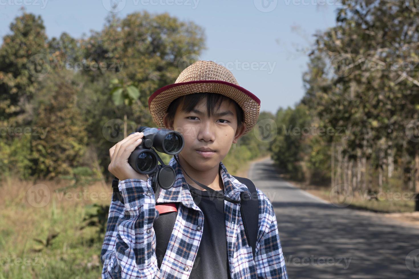Asian boy is using binoculars to do the birds' watching in tropical forest during summer camp, idea for learning creatures and wildlife animals and insects outside the classroom. photo