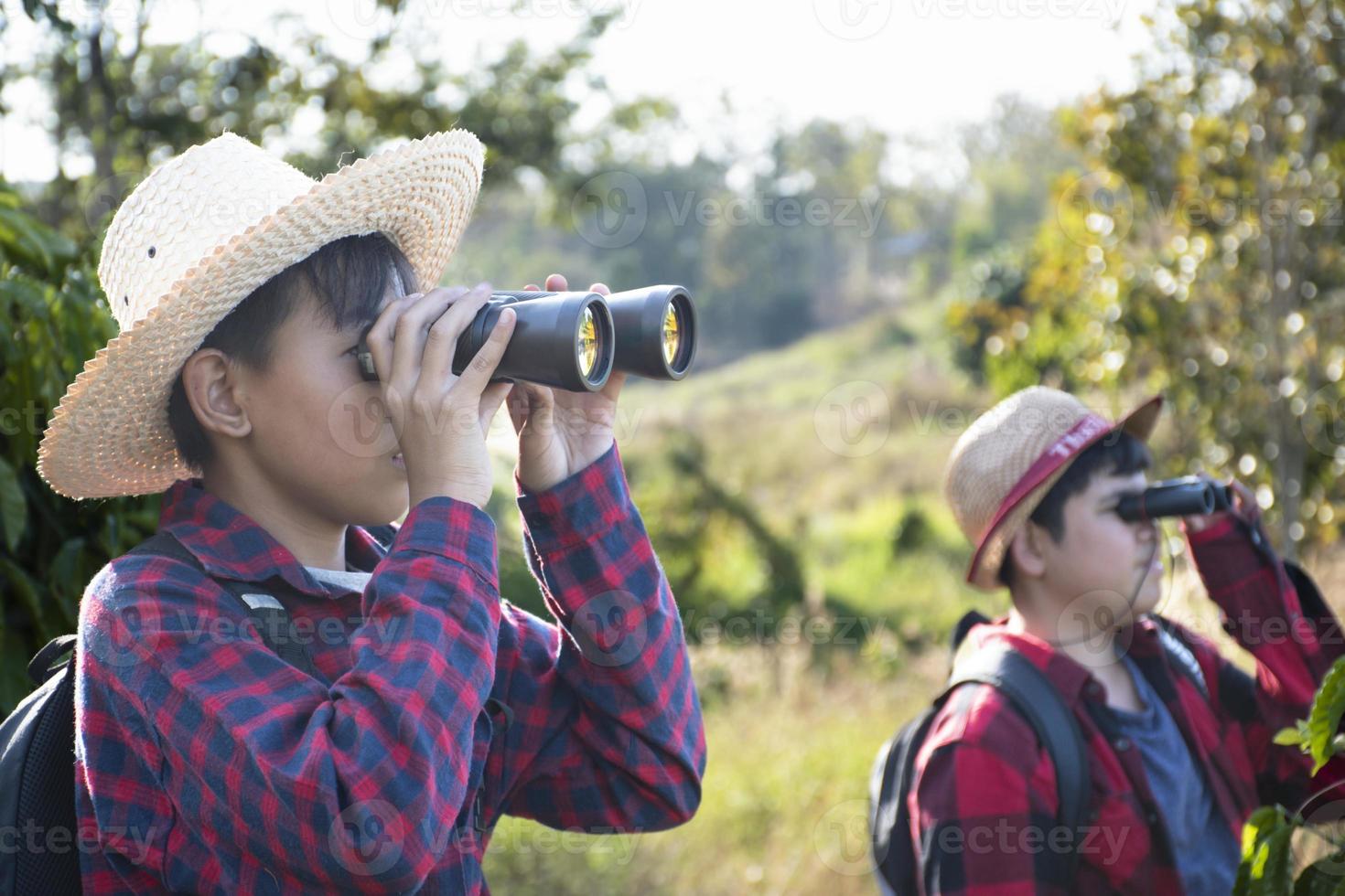 Asian boys are using binoculars to do the birds' watching in tropical forest during summer camp, idea for learning creatures and wildlife animals and insects outside the classroom. photo