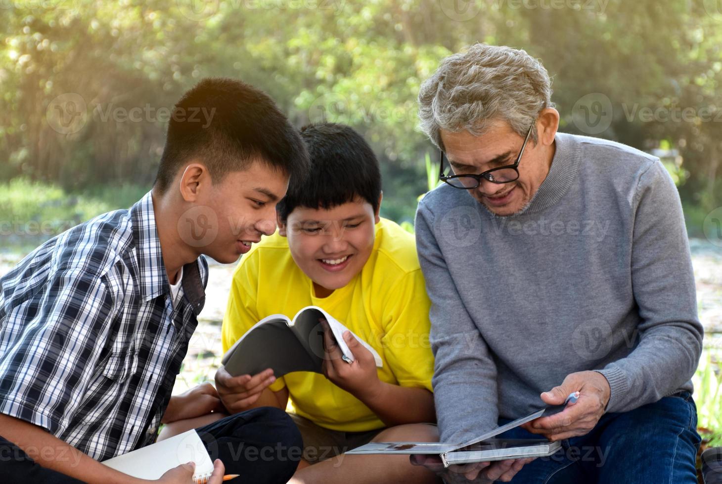 un anciano asiático pasa su tiempo libre explicando el contenido de la lección y felizmente ayudando a sus dos nietos con sus deberes y proyectos escolares en su patio trasero, enfoque suave. foto