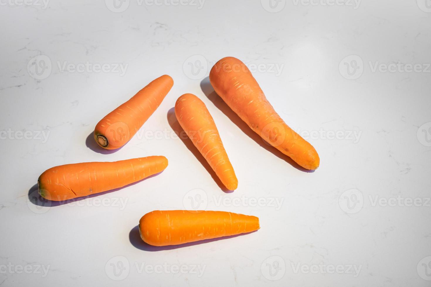 Fresh Carrot lay on white marble top table surface background with hard light and shadow on it. photo