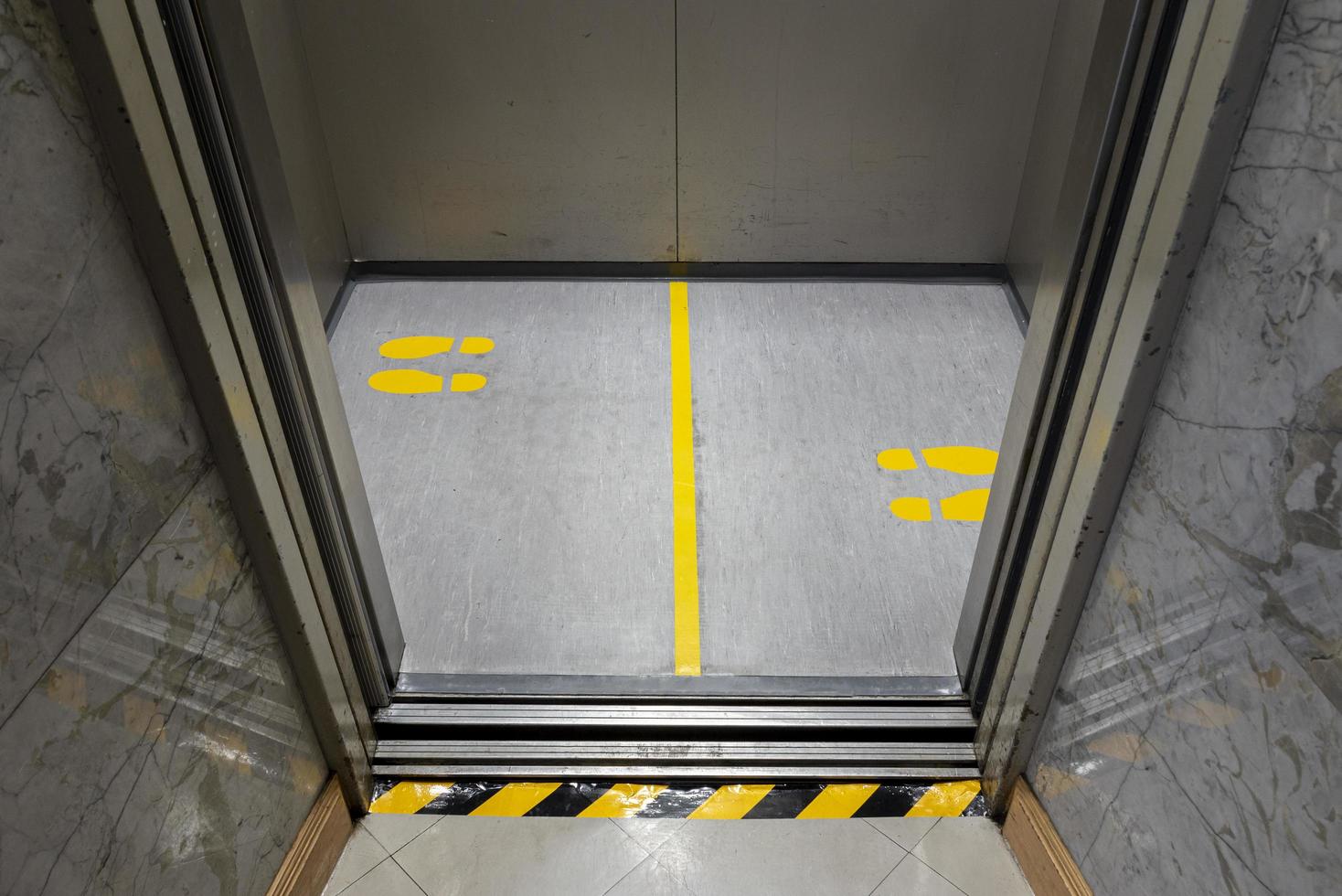 distanciamiento social para covid-19 con señal de huella amarilla en ascensor público foto