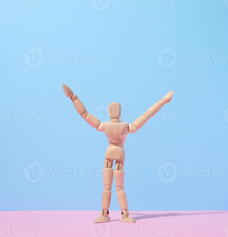 Wooden puppet man on a blue background, arms raised up photo