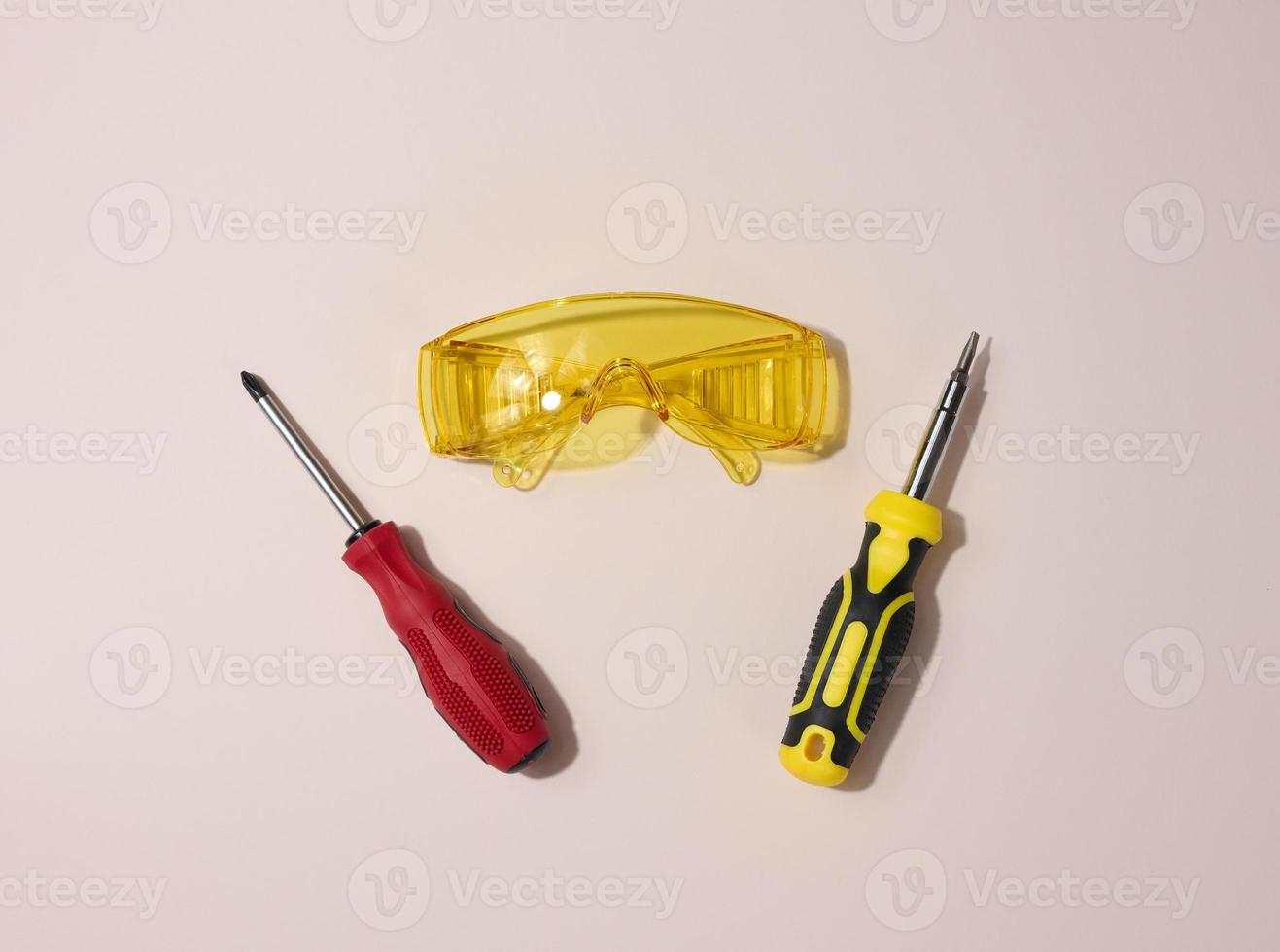 Transparent acrylic glasses and a screwdriver on a beige background, top view photo