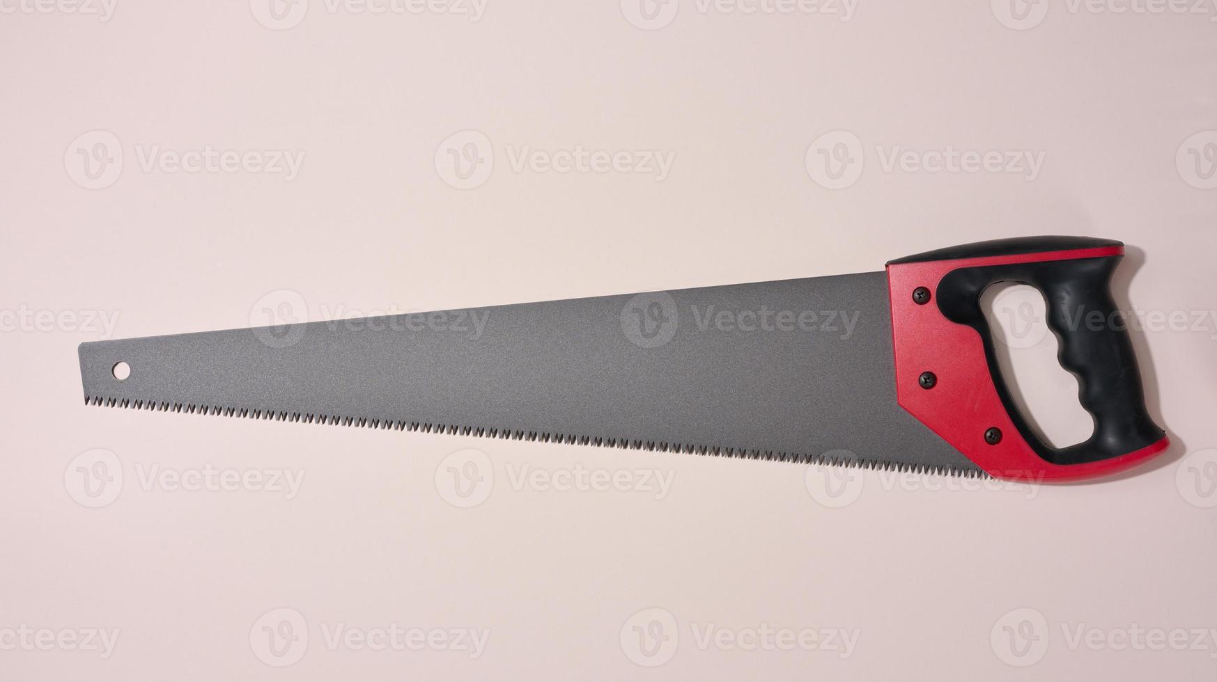 New hand saw with a rubber red handle on a beige background, photo