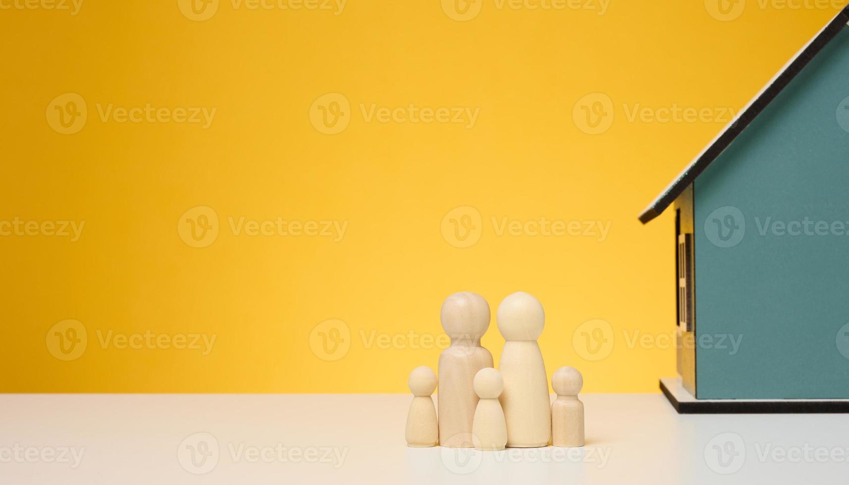 Wooden house and miniature figurines of a family on a yellow background. The concept of selling and buying real estate photo