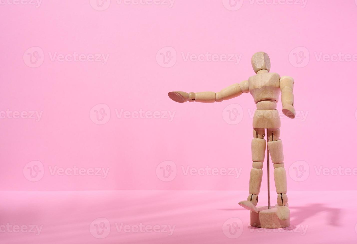 Wooden puppet man on a pink background, pointing with his hand photo