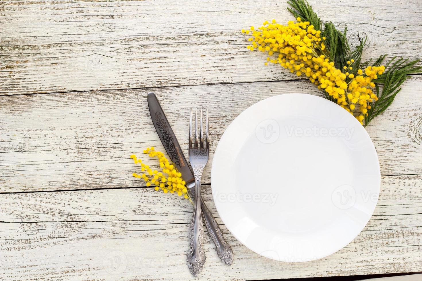 Festive table setting plate with fork and knife and mimosa flower decoration on white wooden background with copy space photo