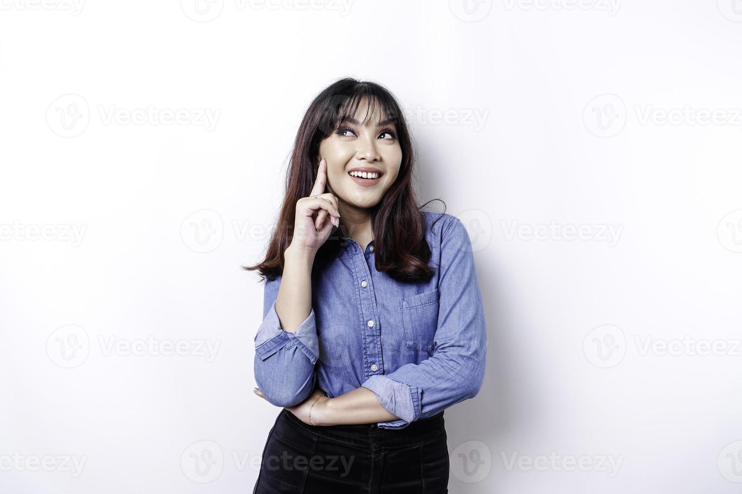 A thoughtful young woman dressed in blue shirt while looking aside, isolated by white background photo