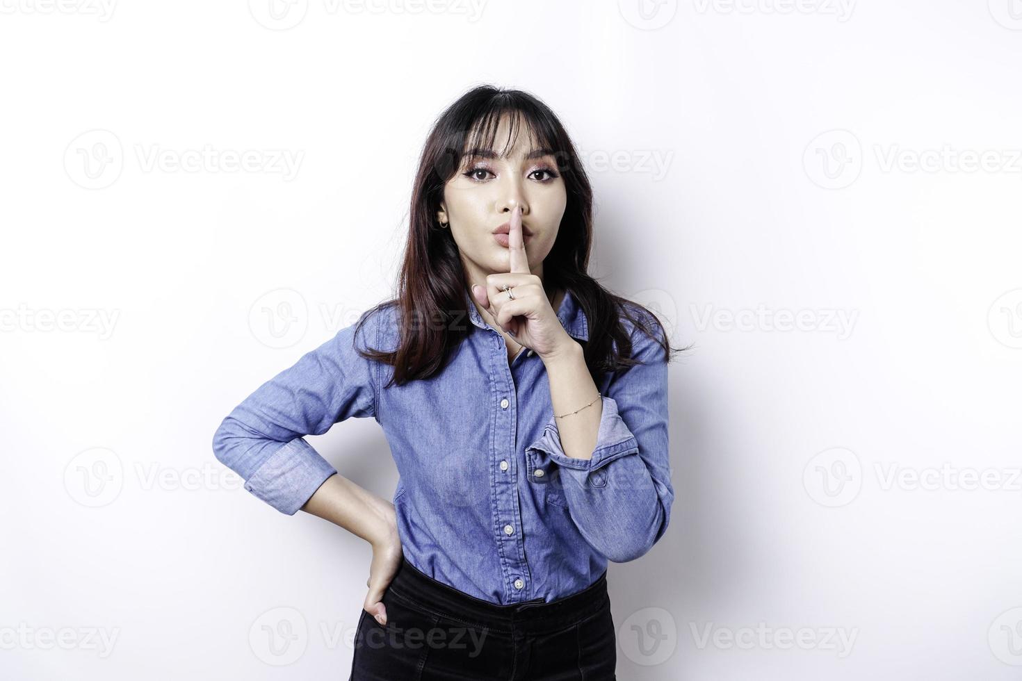 retrato de una joven asiática que se calla, se calla con la cara seria, se calla con el dedo presionado contra los labios, aislada por un fondo blanco foto