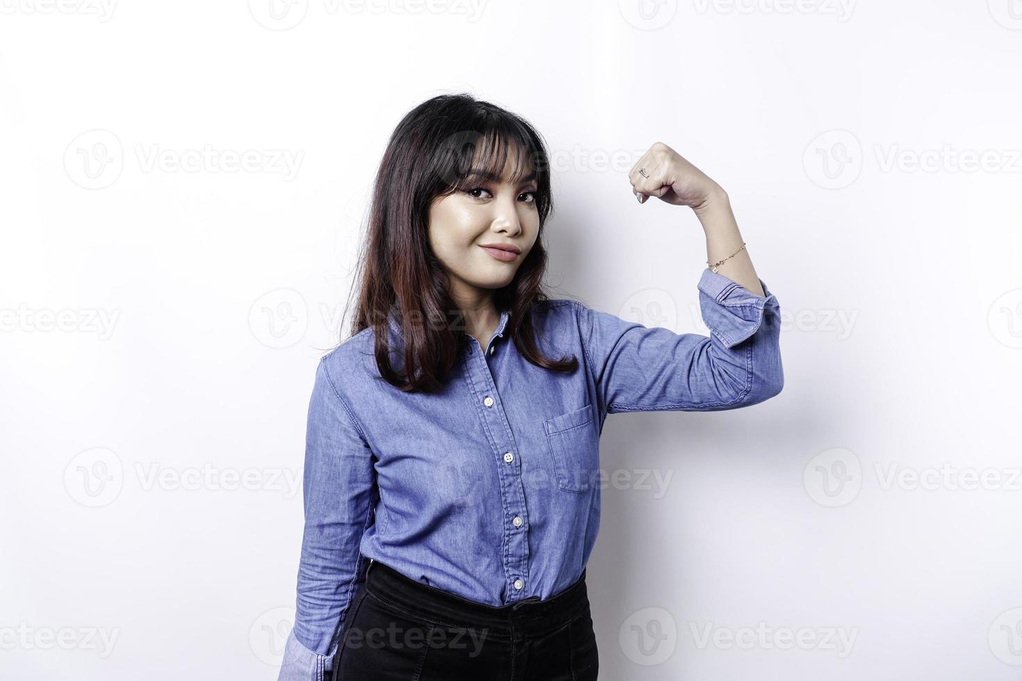 mujer asiática emocionada con una camisa azul que muestra un gesto fuerte levantando los brazos y los músculos sonriendo con orgullo foto