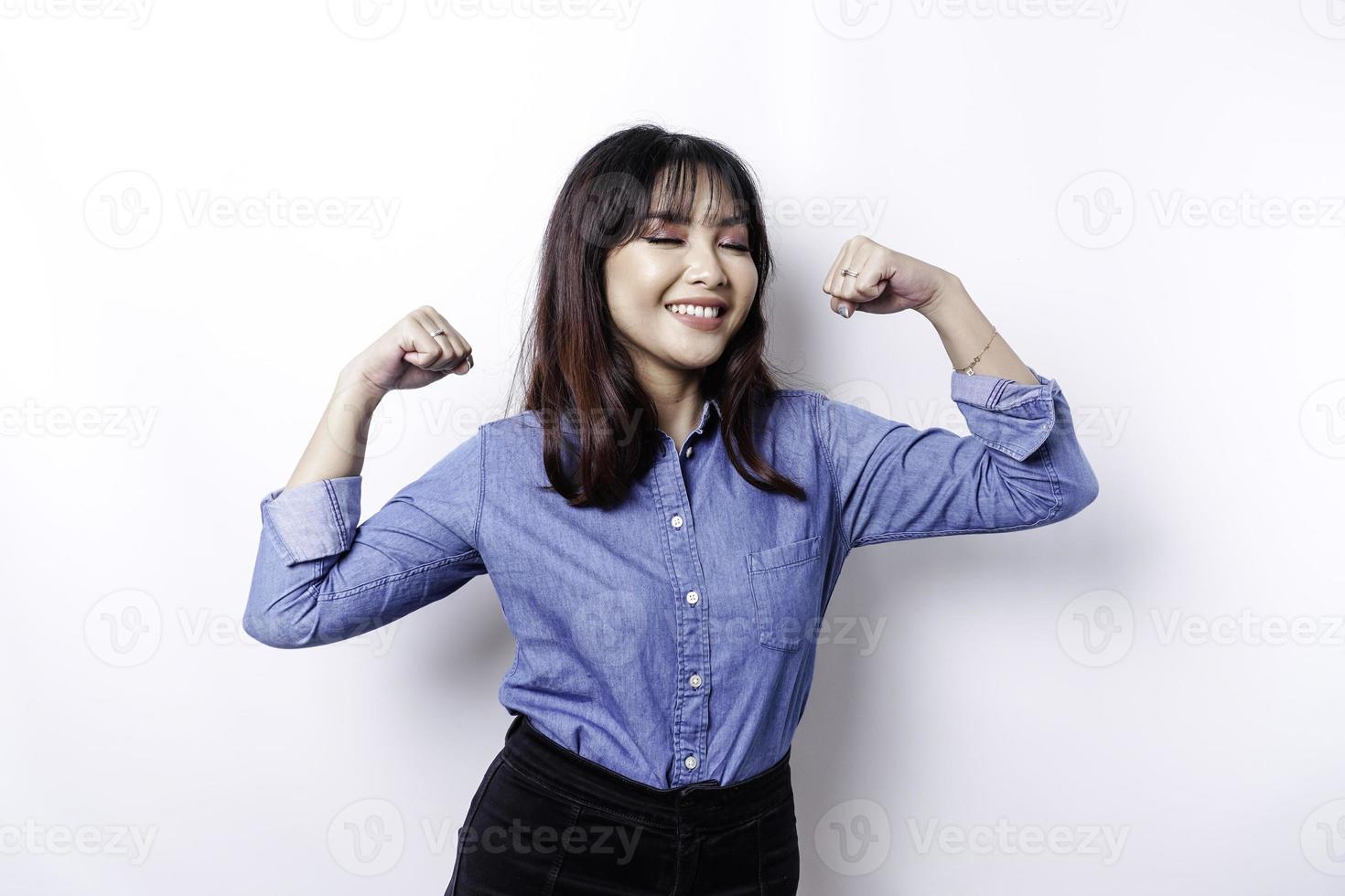 mujer asiática emocionada con una camisa azul que muestra un gesto fuerte levantando los brazos y los músculos sonriendo con orgullo foto
