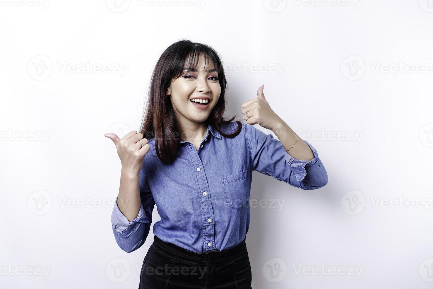 Una mujer asiática emocionada con pantalones azul da un gesto de aprobación con la mano hacia arriba, aislada de fondo blanco foto