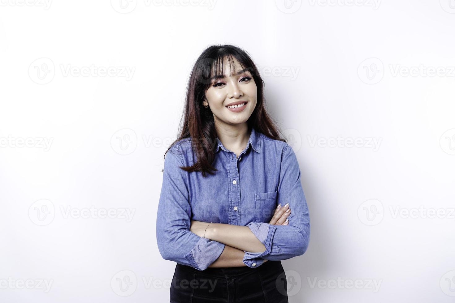 Portrait of a confident smiling Asian woman wearing blue shirt standing with arms folded and looking at the camera isolated over white background photo