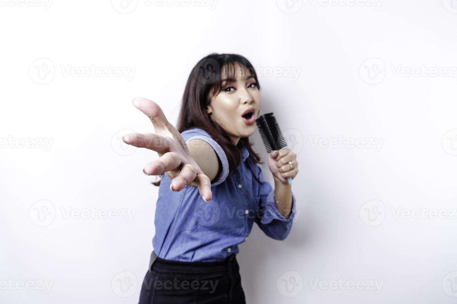 Portrait of carefree Asian woman, having fun karaoke, singing in microphone while standing over white background photo