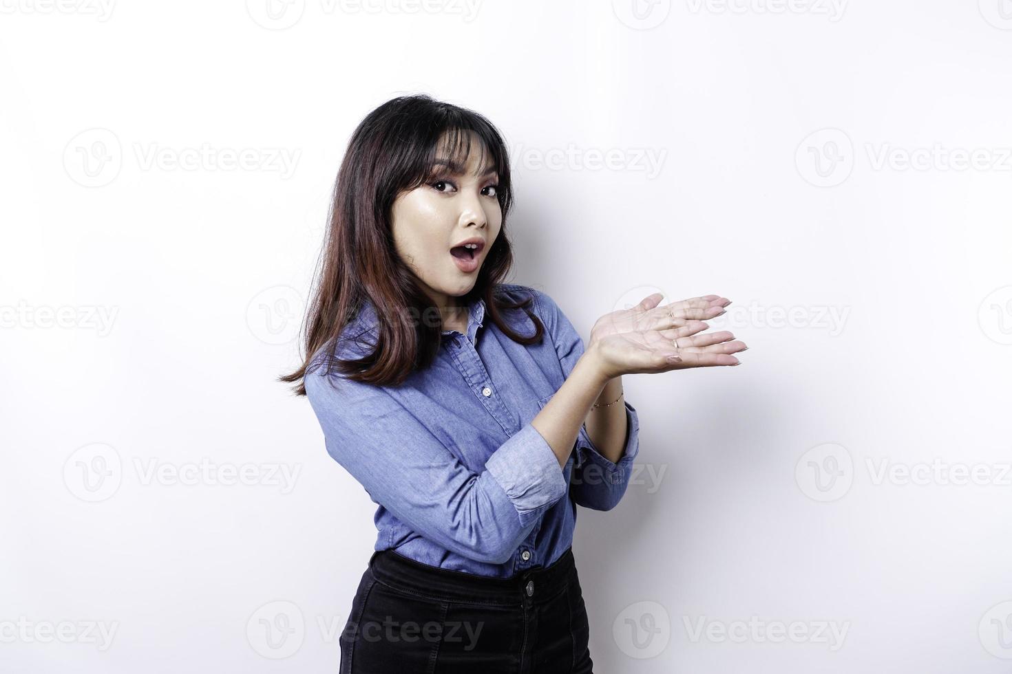 mujer asiática sorprendida con pantalones azul apuntando al espacio de copia a su lado, aislada por fondo blanco foto