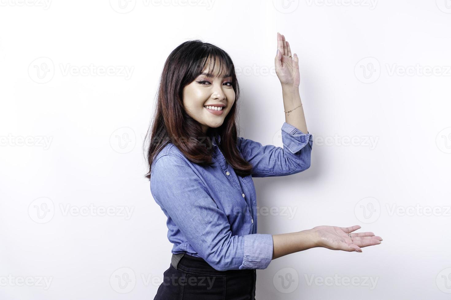 Excited Asian woman wearing blue shirt pointing at the copy space beside her, isolated by white background photo