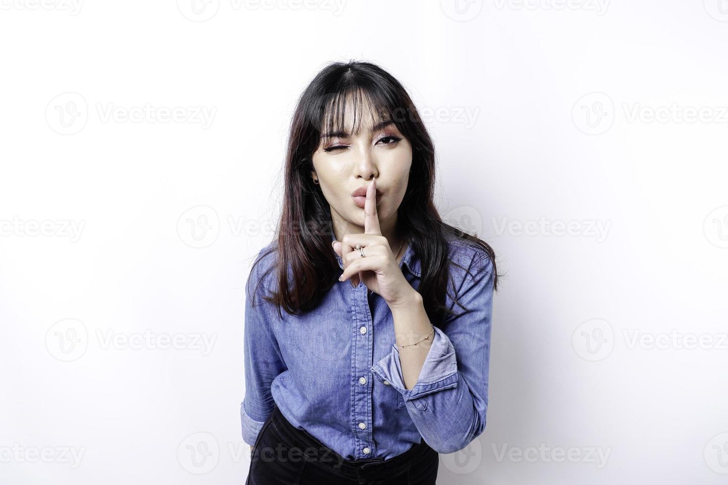 Portrait of a young Asian woman tell be quiet, shushing with serious face, hush with finger pressed to lips, isolated by white background photo