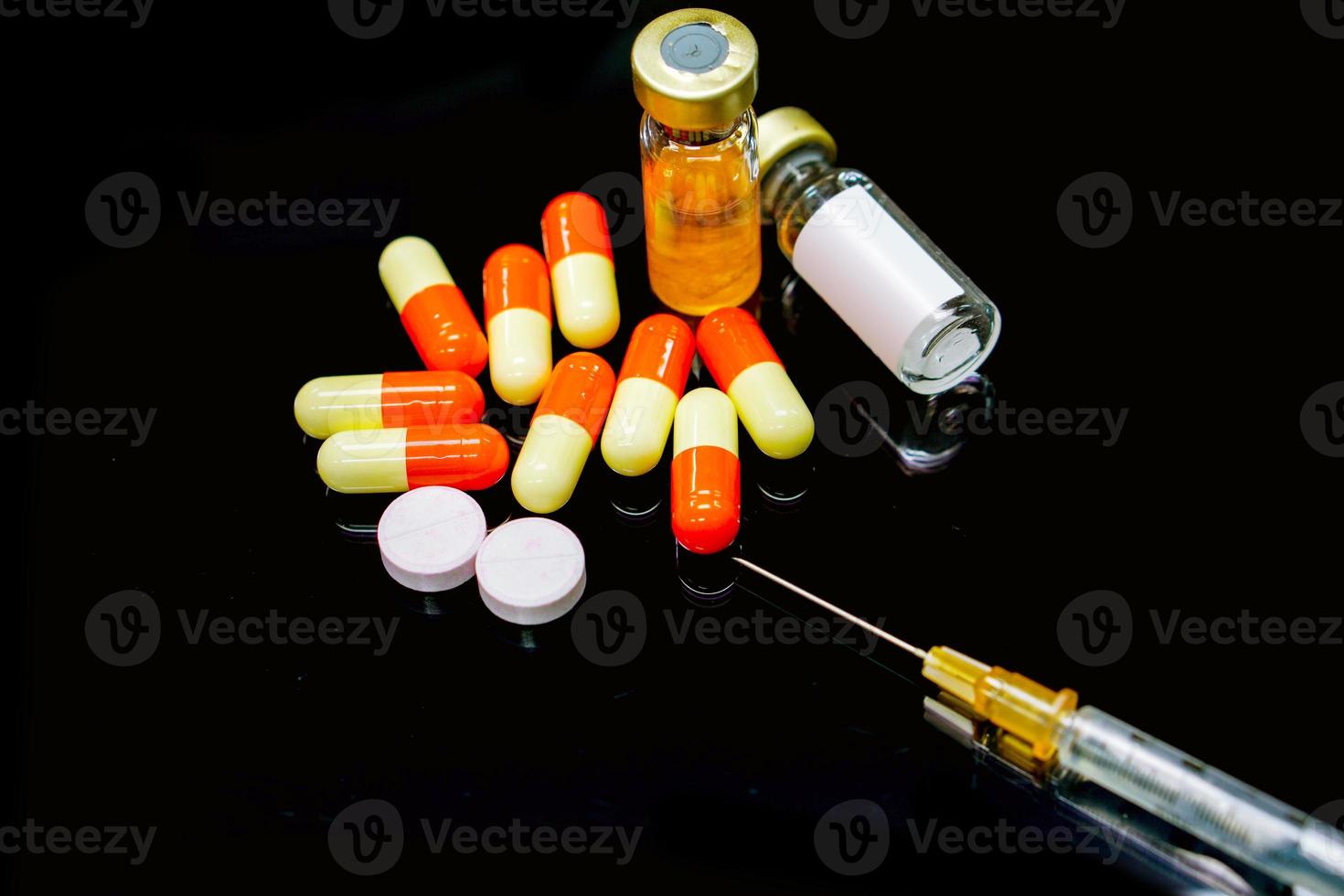 jeringa de plástico, medicamentos en cápsula, medicamento inyectable en viales, medicamentos de píldora blanca y roja aislados sobre fondo negro. foto