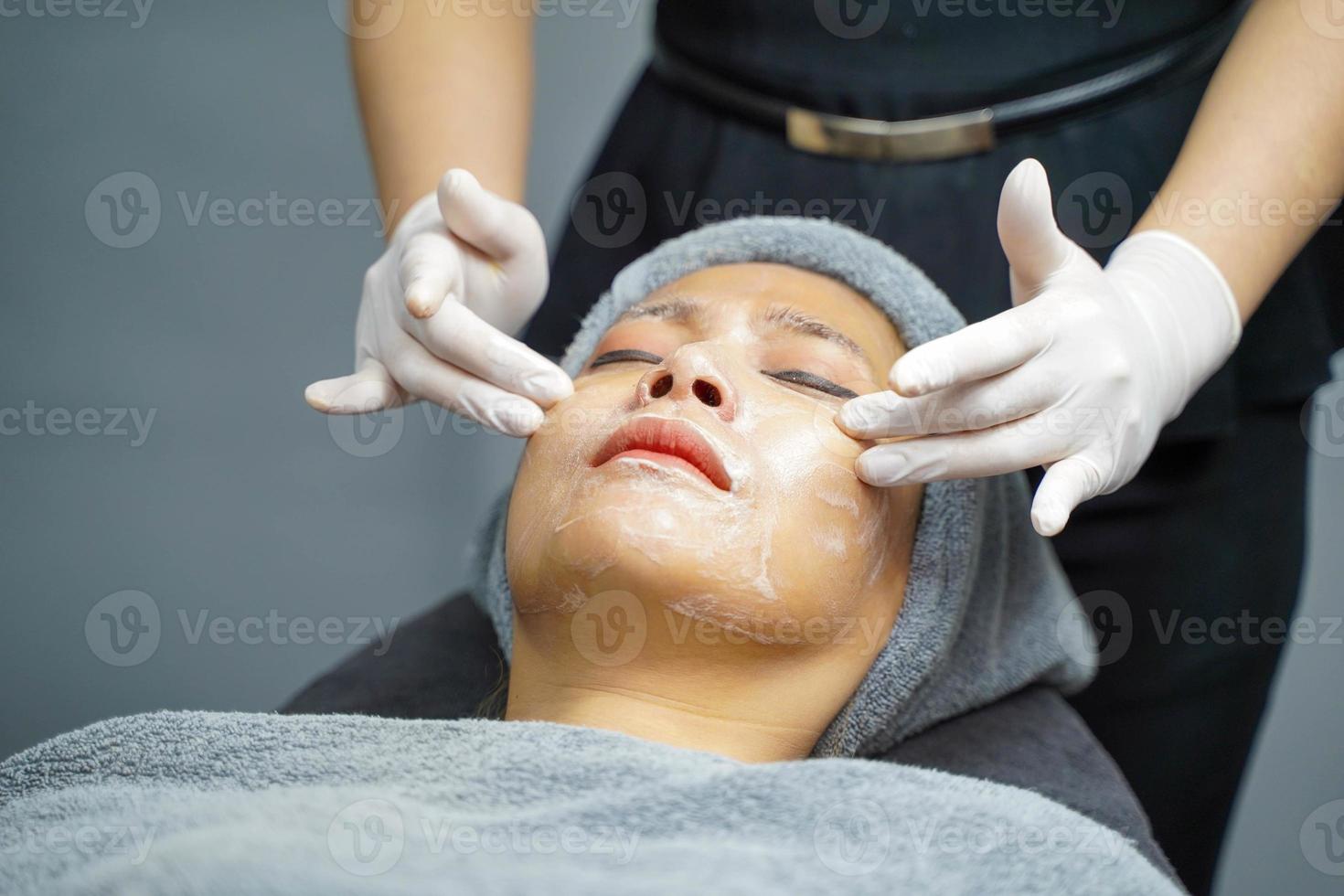 mujer joven belleza en toalla haciendo masaje facial con exfoliante facial orgánico. foto