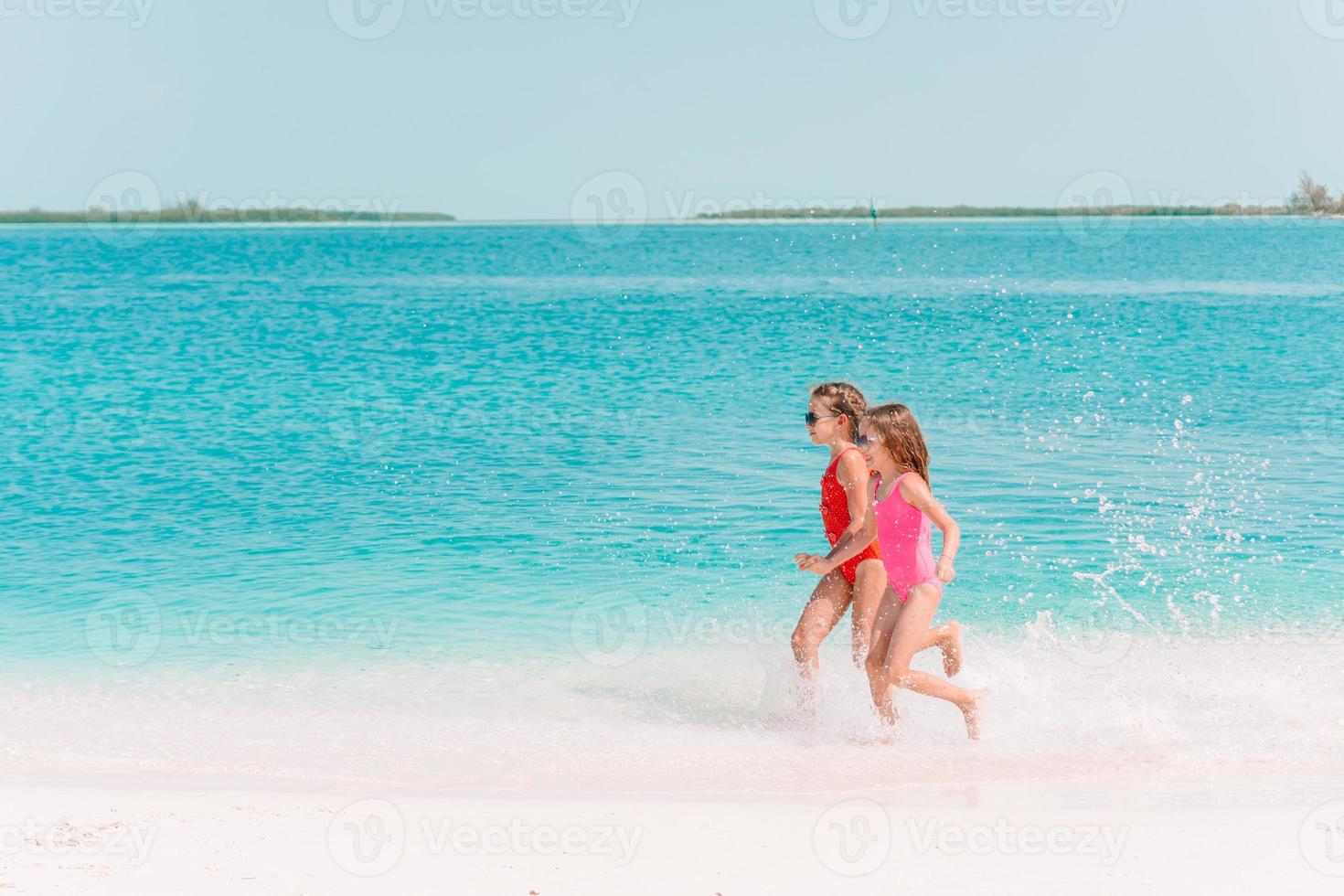 Little happy funny girls have a lot of fun at tropical beach playing together. photo