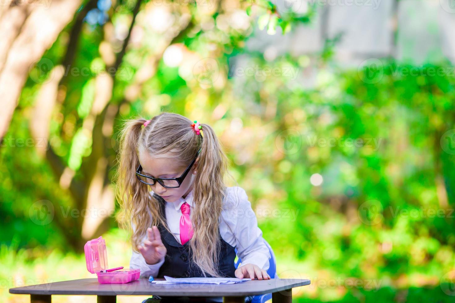 Clever little school girl at desk with notes and pencils outdoor. Back to school. photo