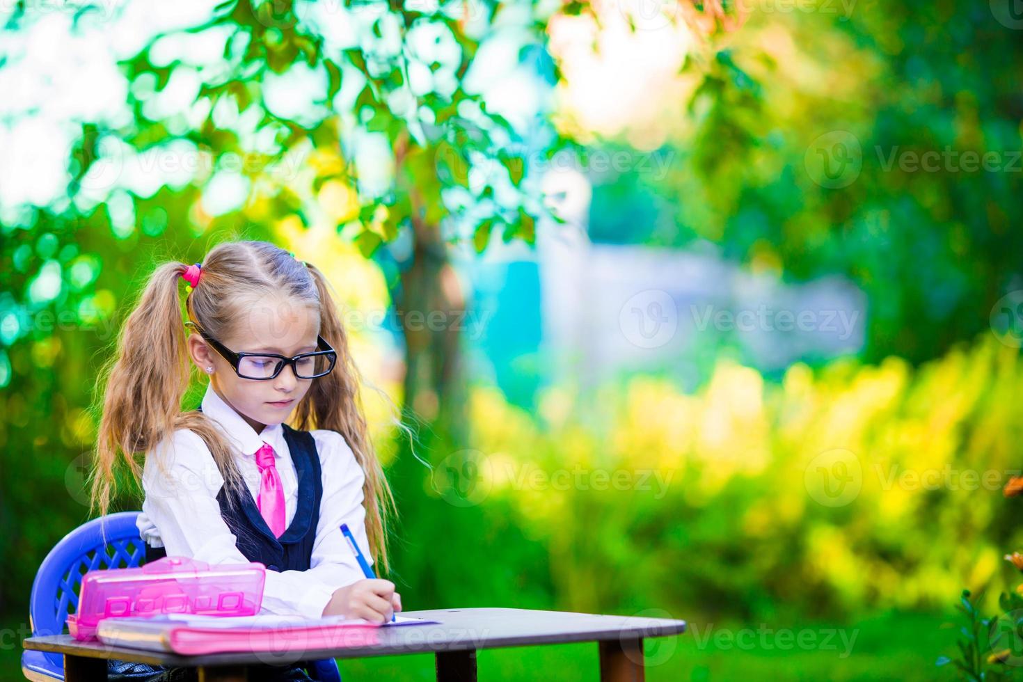 Cute little school girl writing at desk with pencil outdoor. Back to school. photo