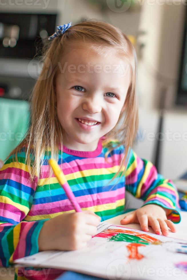 Adorable little girl draws paints sitting at the table photo