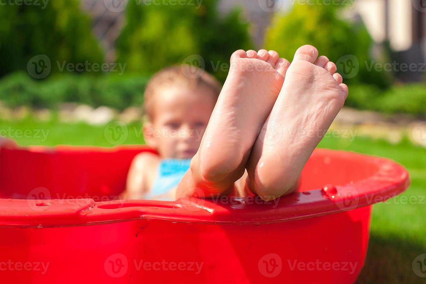 Closeup of little kid's legs in small red pool photo