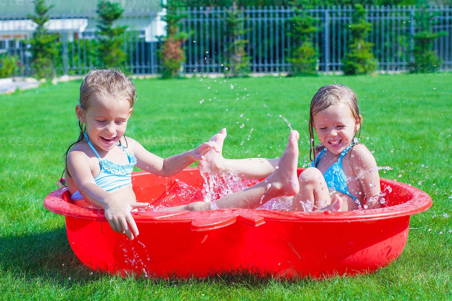 Two little sisters playing and splashing in the pool on a hot sunny day photo