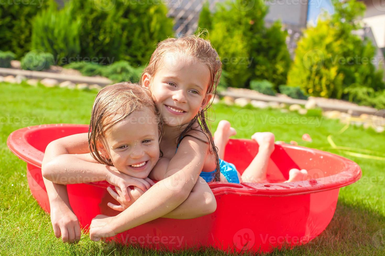 Two little sisters playing and splashing in the pool on a hot sunny day photo