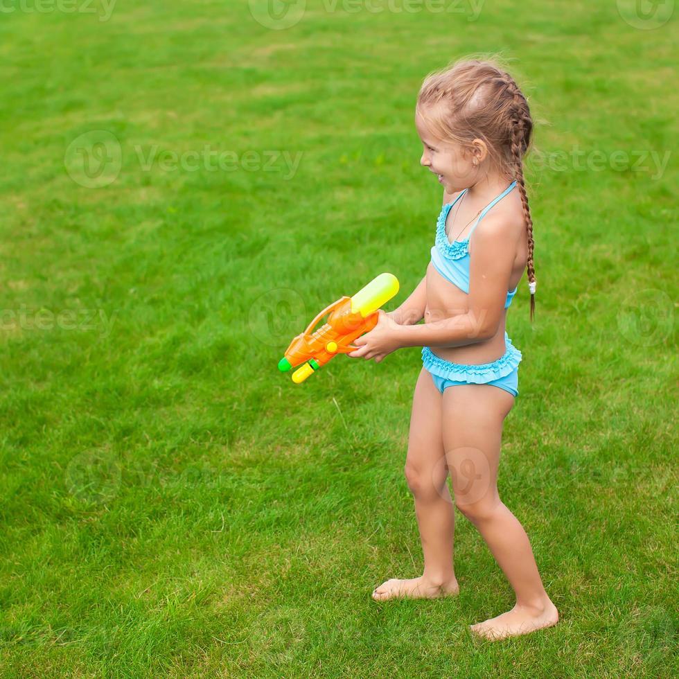 Little adorable girl playing with water gun outdoor in sunny summer day photo