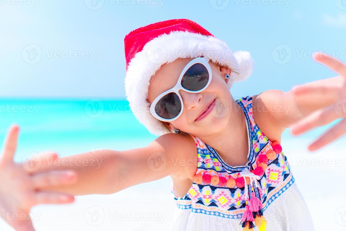 adorable niña con sombrero de santa durante las vacaciones navideñas en la playa foto