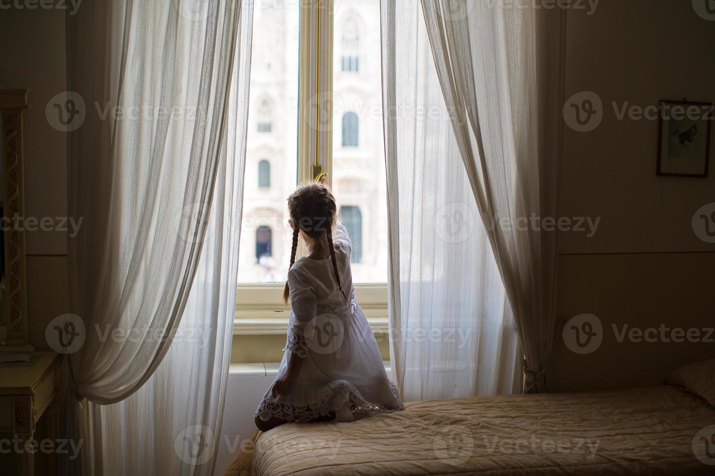 adorable niña mirando por la ventana al duomo, milán, italia foto