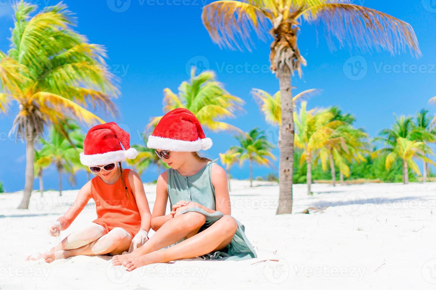 niñas adorables con sombreros de santa durante las vacaciones en la playa se divierten juntas foto