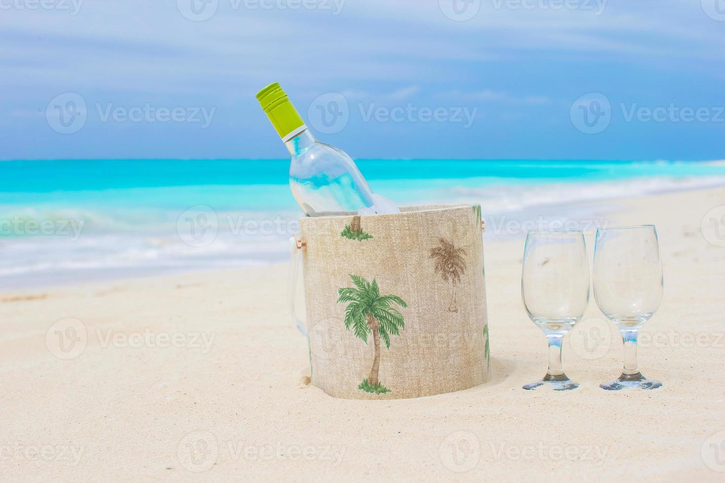 Bottle of white wine and two glasses on the exotic sandy beach photo