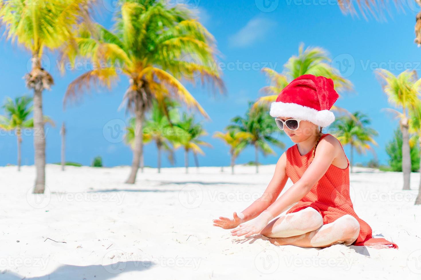 Adorable little girl in Santa hat during Christmas beach vacation photo