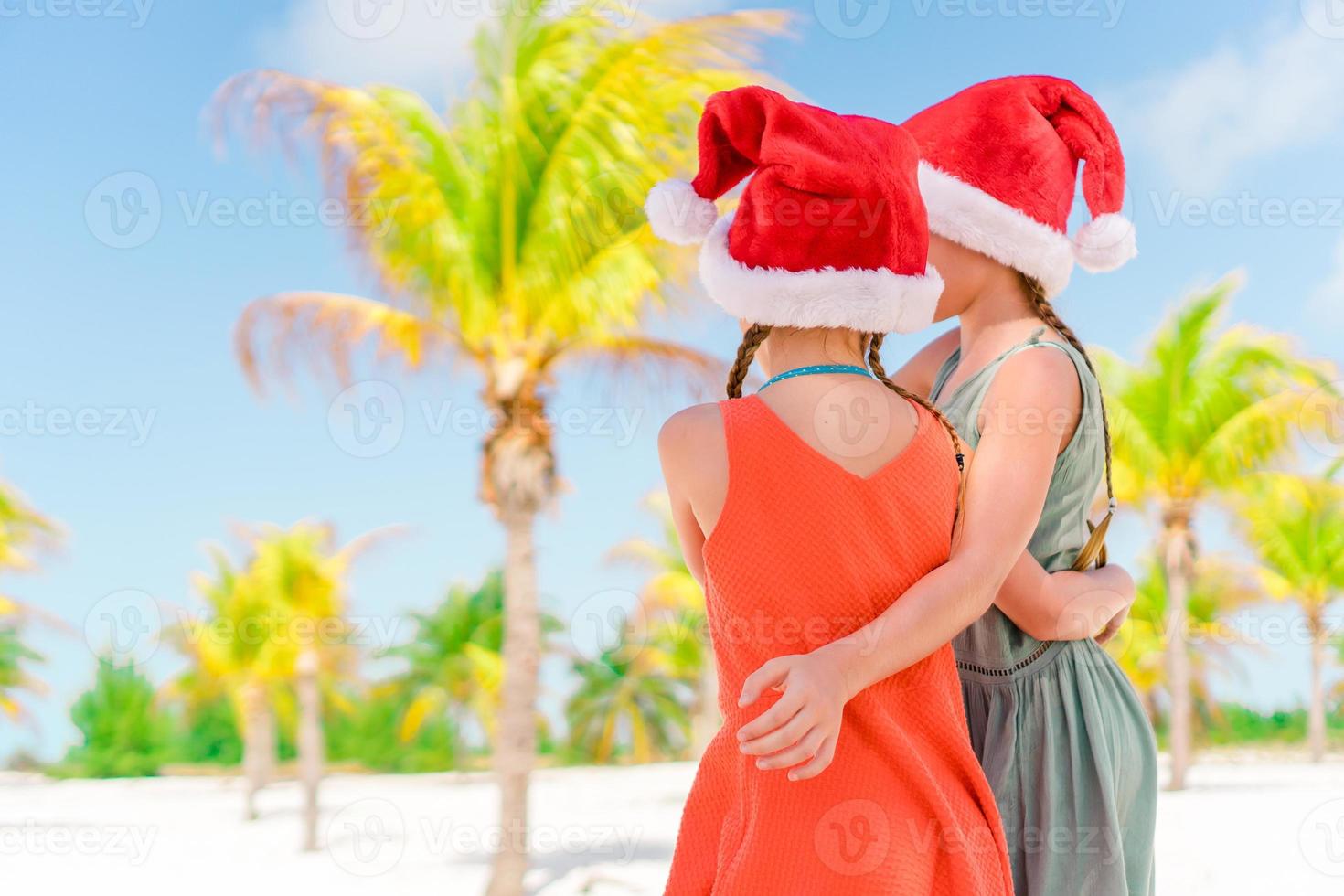 Little adorable girls in Santa hats during beach vacation have fun together photo