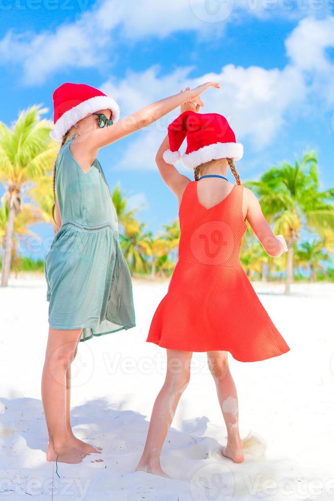 Little adorable girls in Santa hats during beach vacation have fun together photo